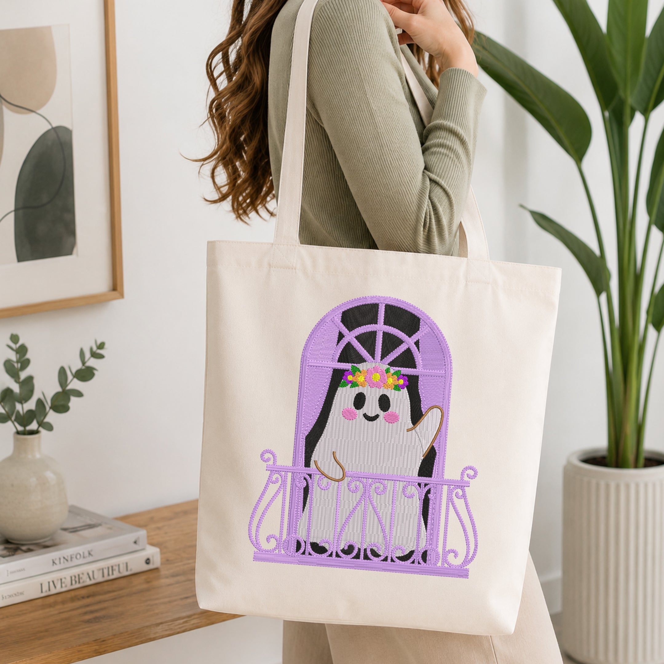 A woman holds a cream canvas tote bag with a purple arched window design featuring a cute penguin character. The scene is set in a bright, modern room with a wooden table, books, and a potted plant.