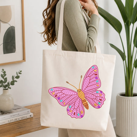 A person carrying a cream-colored canvas tote bag that is decorated with the same pink butterfly embroidery design.