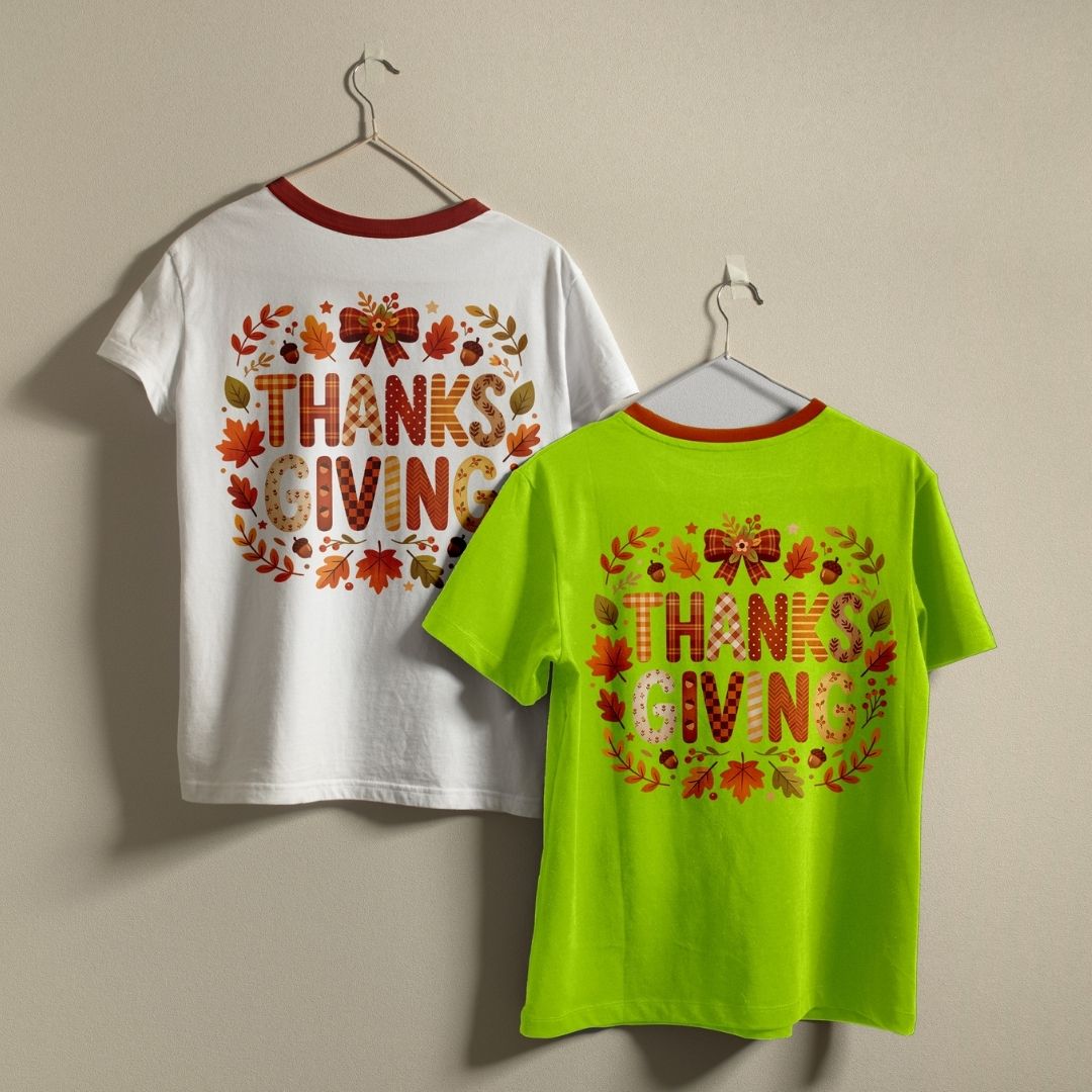Two short-sleeve ringer T-shirts hanging on hangers against a plain beige wall, showing the back designs. One shirt is white with a red collar and a large 'THANKSGIVING' graphic made of autumn leaves and acorns.