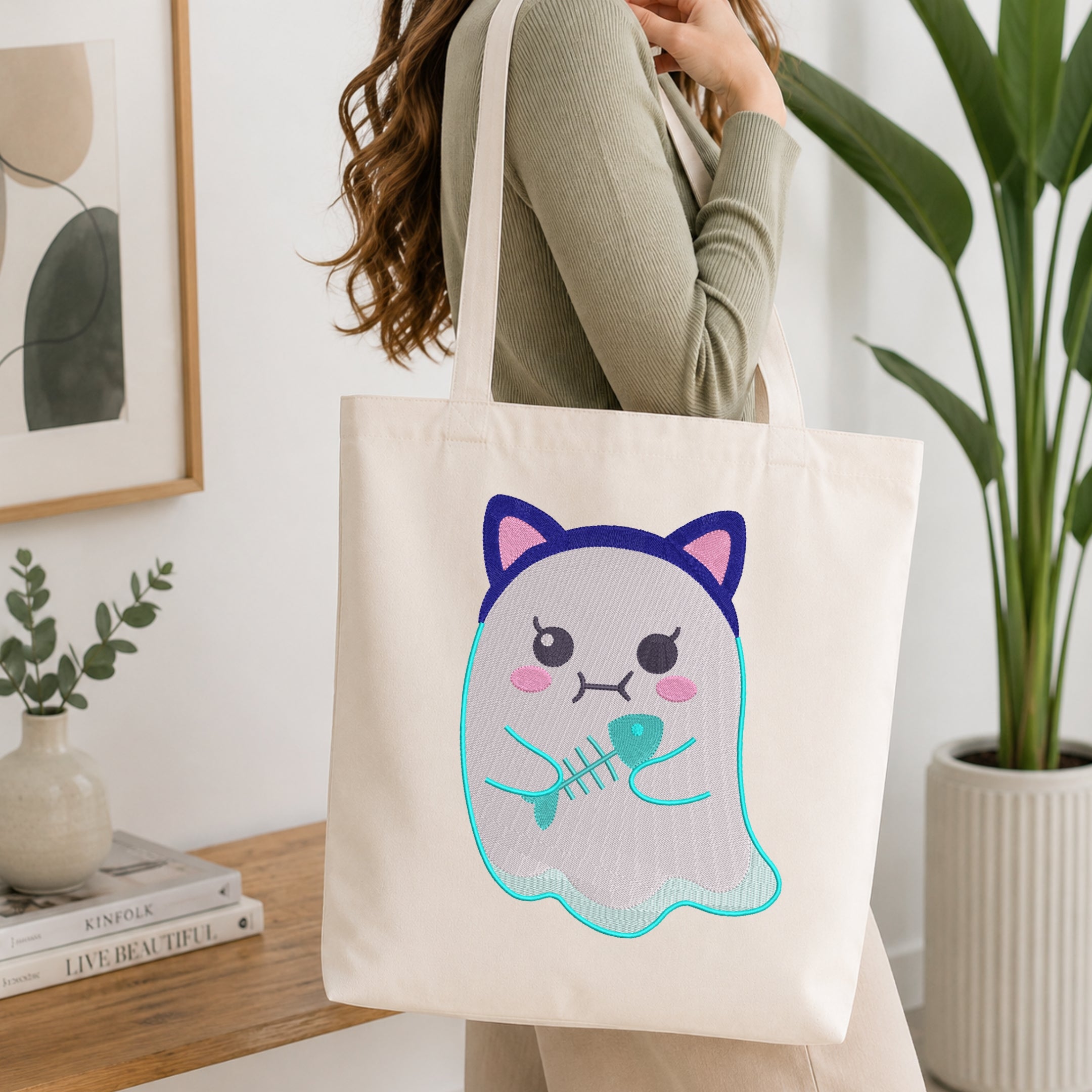 A woman carrying a canvas tote bag embroidered with a cute ghost wearing cat ears and holding a fish skeleton in a brightly lit room.