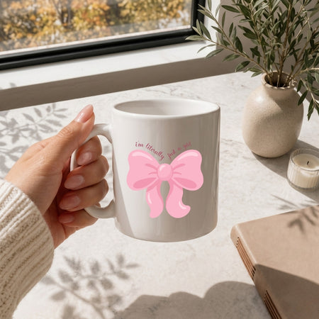Hand holding a white ceramic coffee mug featuring the pink bow design.
