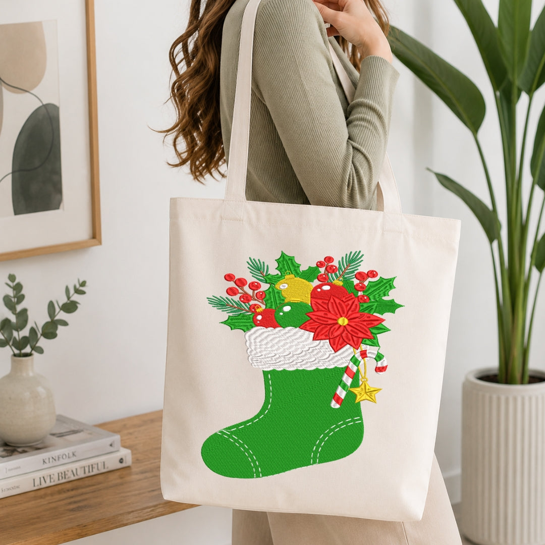 A woman wearing a ribbed sage green long-sleeve top carries a cream canvas tote bag decorated with a festive Christmas stocking graphic. The graphic features a green stocking filled with red poinsettias, holly leaves, green pine branches, a yellow ornament, and candy canes.