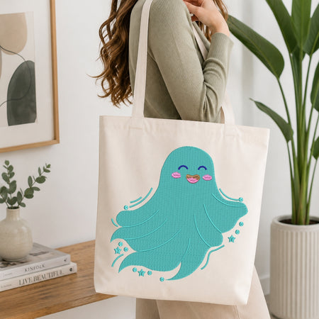 A woman wearing a sage green ribbed sweater carries a cream canvas tote bag featuring a cute, smiling turquoise octopus with pink cheeks and blue star accents, set against a bright, modern room background with a wooden table, books, and a potted plant.