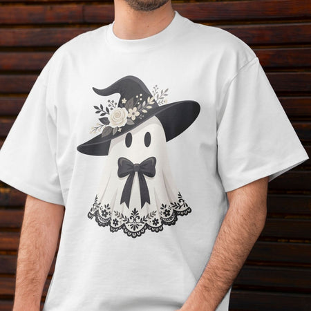 Hand holding a white coffee mug printed with a cute floral ghost wearing a witch hat against a warm background.