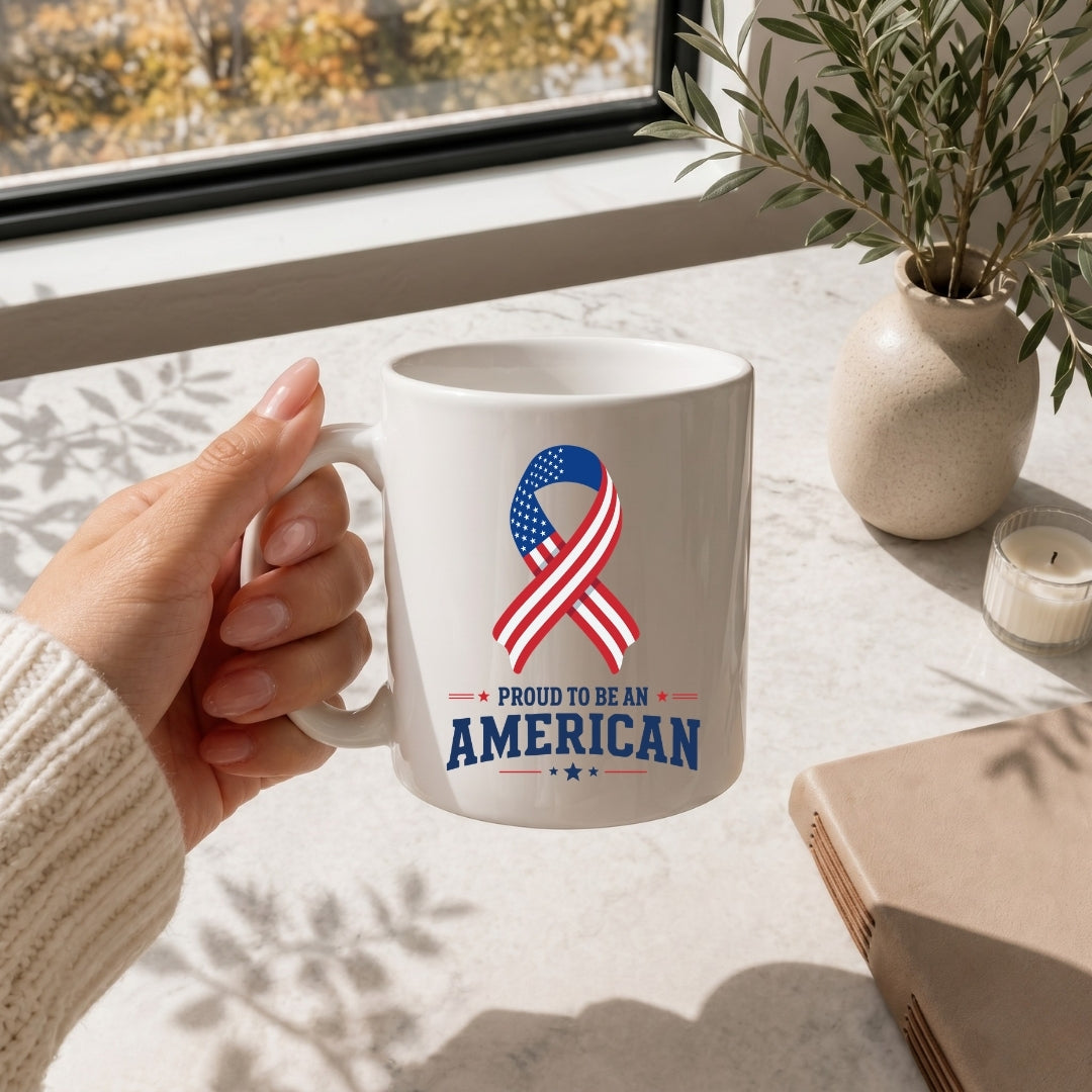 A hand holding a white ceramic mug featuring an American flag ribbon graphic and the text "Proud to be an American."