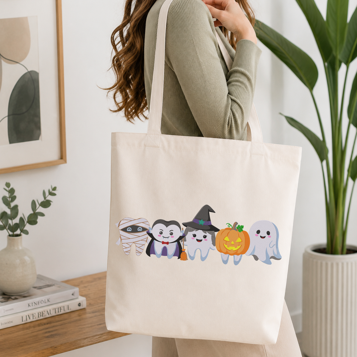 Woman carrying a white natural canvas tote bag featuring a cute Halloween dental teeth characters machine embroidery design in a bright, modern interior setting