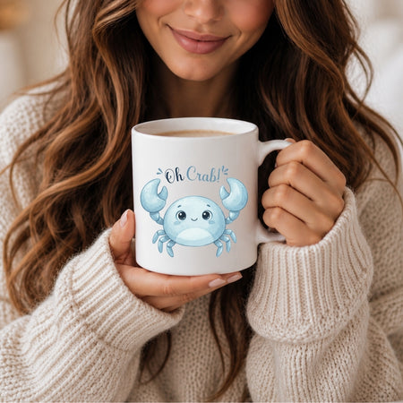 A woman with long brown hair holding a white ceramic mug featuring a blue cartoon crab graphic and the text "Oh Crab!"