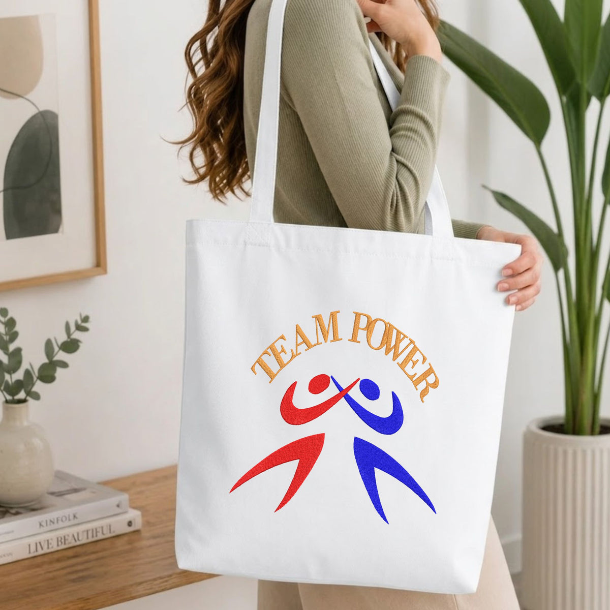 Woman carrying a white natural canvas tote bag featuring an embroidered "Team Power" design in a bright, modern interior setting   