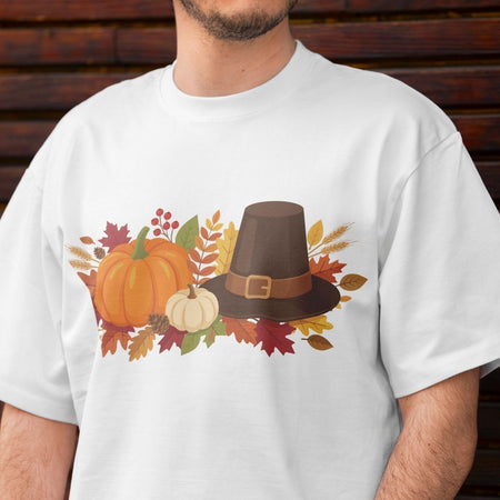 White t-shirt with a Thanksgiving design featuring pumpkins, a pilgrim hat, and leaves on a wooden background.