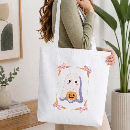 Woman carrying a white natural canvas tote bag featuring a cute ghost machine embroidery design in a bright, modern interior setting