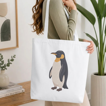  Woman carrying a white natural canvas tote bag featuring an embroidered penguin design in a bright, modern interior setting   
