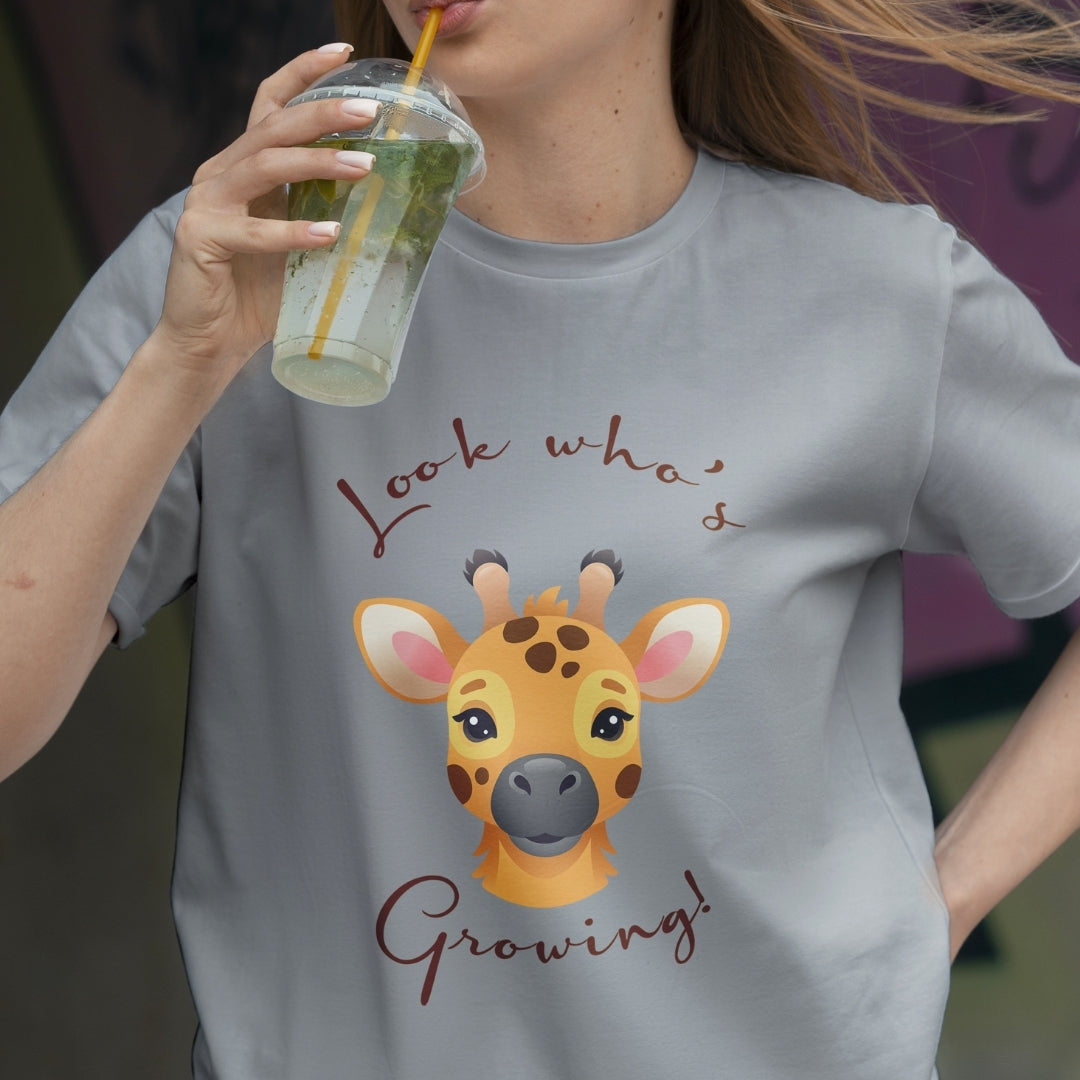 Person wearing a t-shirt with a giraffe graphic and text, holding a drink.