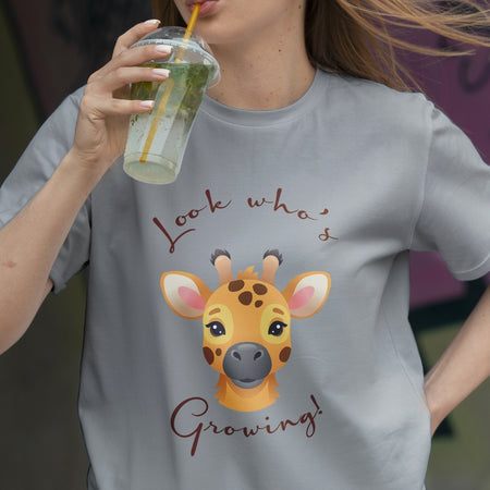 Person wearing a t-shirt with a giraffe graphic and text, holding a drink.