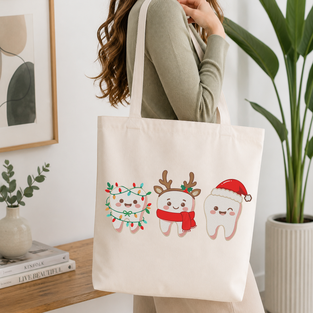 Woman carrying a white natural canvas tote bag featuring a cute Christmas teeth characters machine embroidery design in a bright, modern interior setting