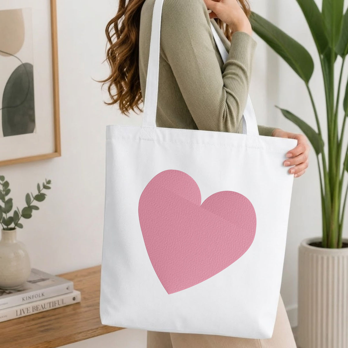Woman carrying a white natural canvas tote bag featuring a minimalist heart machine embroidery design in a bright, modern interior setting