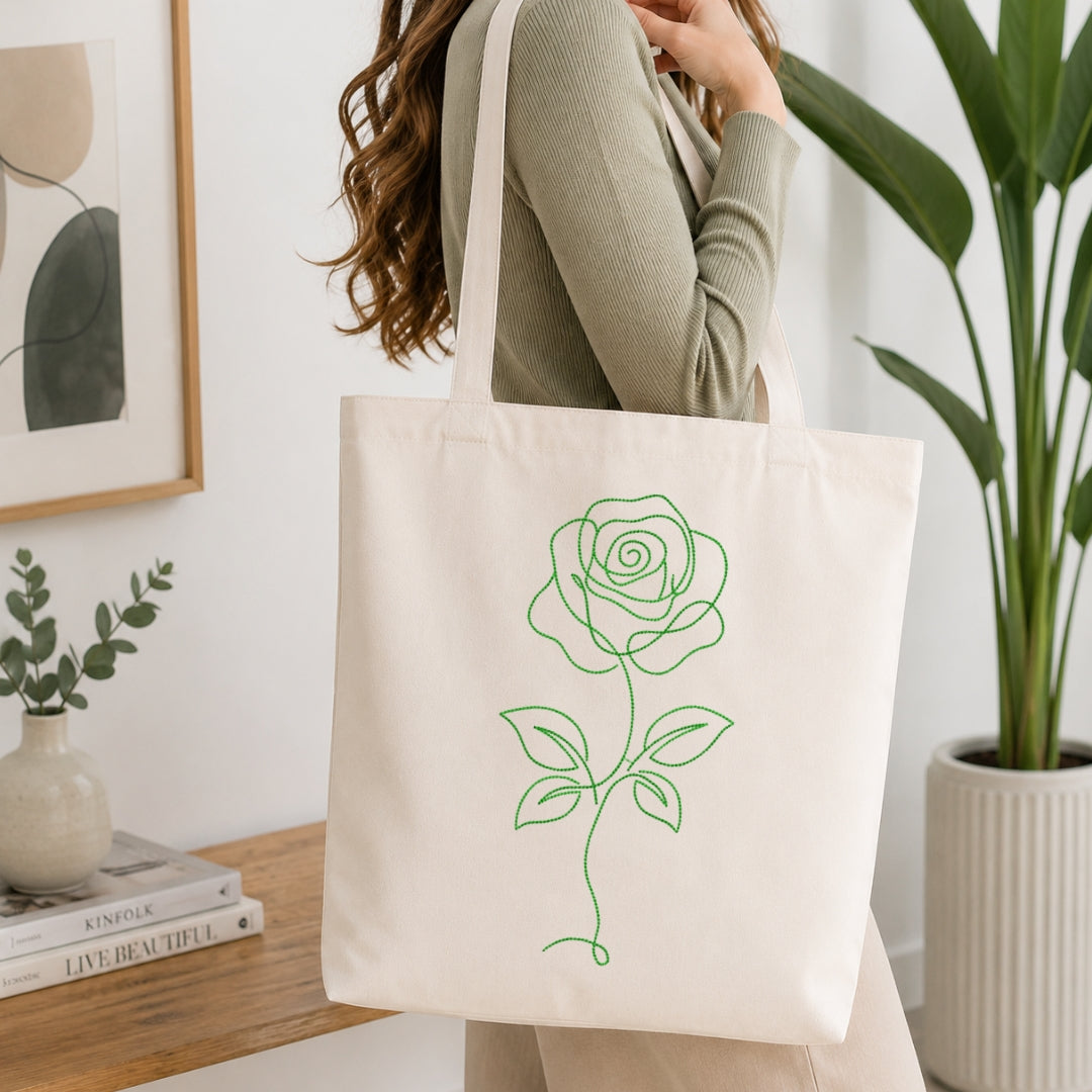 A woman carrying a canvas tote bag featuring a green line art rose machine embroidery design.