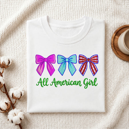 Folded white t-shirt mockup with three embroidered bows and green script text reading All American Girl.