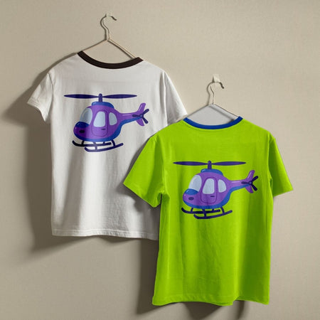 Two children's ringer t-shirts hanging on hangers against a plain beige wall. The left shirt is white with a dark brown collar and features a purple and blue helicopter graphic on the back.