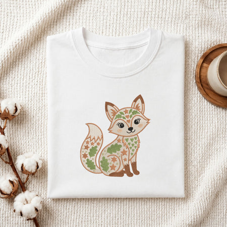 Folded white cotton t-shirt mockup featuring a cute folk art fox machine embroidery design, styled with cotton stems and a wooden cup.   