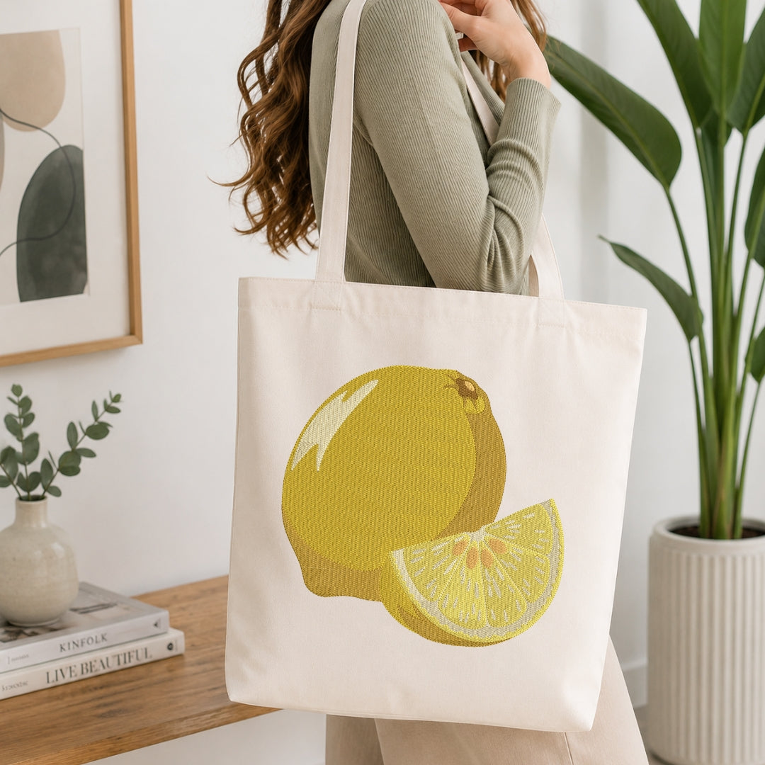 A person carrying a cream canvas tote bag decorated with the embroidered lemon design.