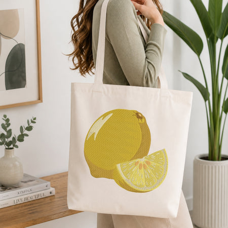 A person carrying a cream canvas tote bag decorated with the embroidered lemon design.