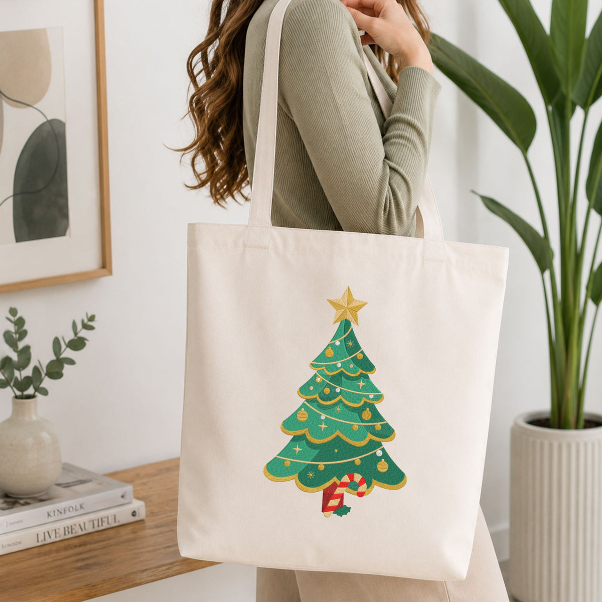 Woman carrying a white natural canvas tote bag featuring a decorated Christmas tree machine embroidery design in a bright, modern interior setting   
