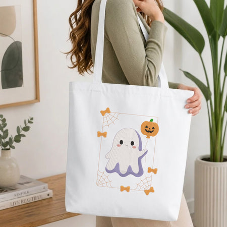 Woman carrying a white natural canvas tote bag featuring a cute ghost machine embroidery design in a bright, modern interior setting