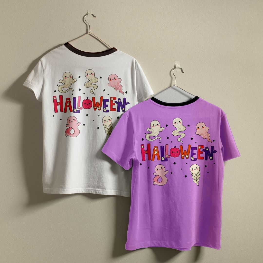 Two children's ringer t-shirts with Halloween graphics, hanging on metal hangers against a plain beige wall. The back of a white shirt shows a ghost pattern and 'HALLOWEEN' text, while the front of a purple shirt shows the same design.