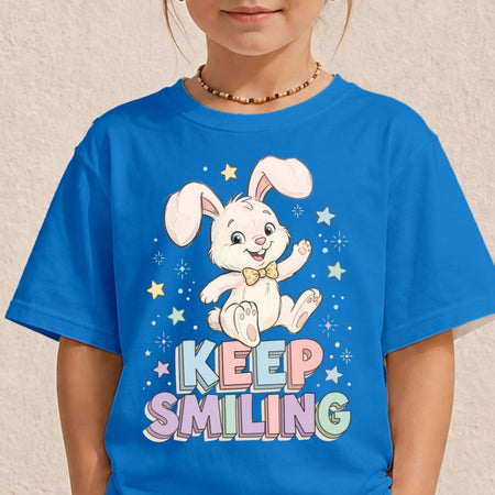 A child wearing a bright blue short-sleeve T-shirt with a cartoon bunny graphic and the words 'KEEP SMILING' in pastel letters. The photo is cropped from the lower face to the torso against a light textured wall.