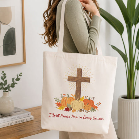 Woman carrying a white natural canvas tote bag featuring a Christian cross and autumn pumpkins machine embroidery design in a bright, modern interior setting