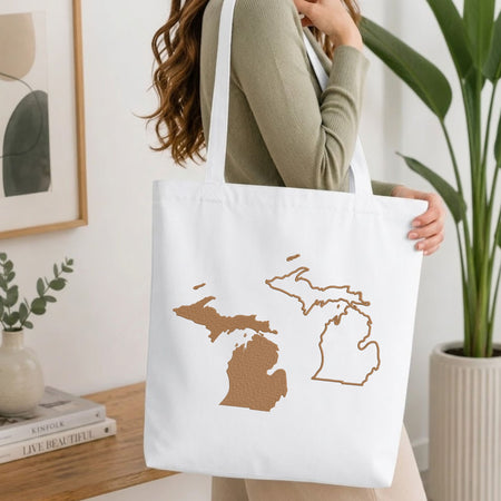 Folded white cotton t-shirt mockup featuring Michigan state map machine embroidery designs, styled with cotton stems and a wooden cup.   