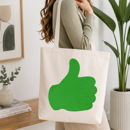 Person holding a tote bag with a green thumbs-up design in a home setting.