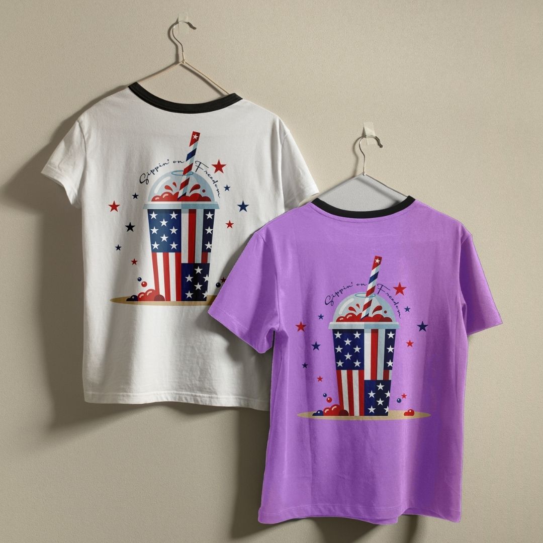A white ringer t-shirt with a black collar and a solid purple t-shirt hanging on a wall, showcasing the custom 4th of July design.
