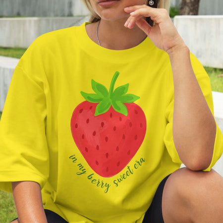Person wearing a yellow t-shirt with a strawberry graphic and text.