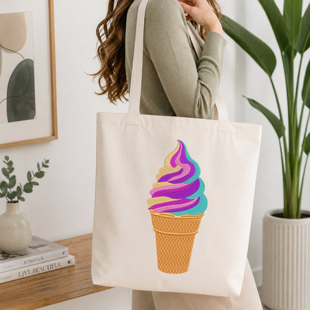 A person wearing a sage green ribbed long-sleeve top carries a cream canvas tote bag with a colorful ice cream cone graphic. The background is a bright, modern room with a wooden table, books, a framed print, and a potted plant.