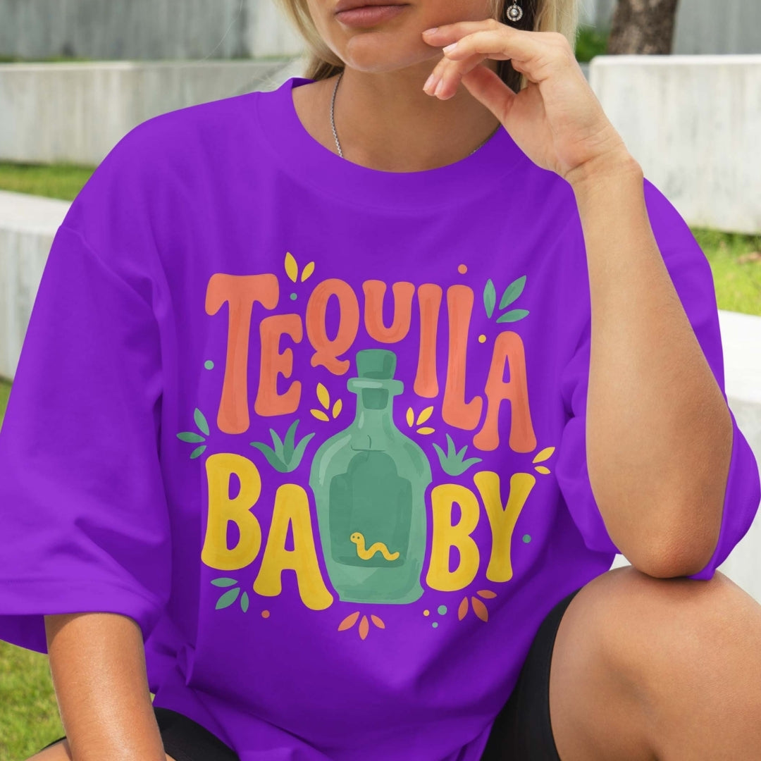 Person wearing a purple t-shirt with 'Tequila Baby' design outdoors.