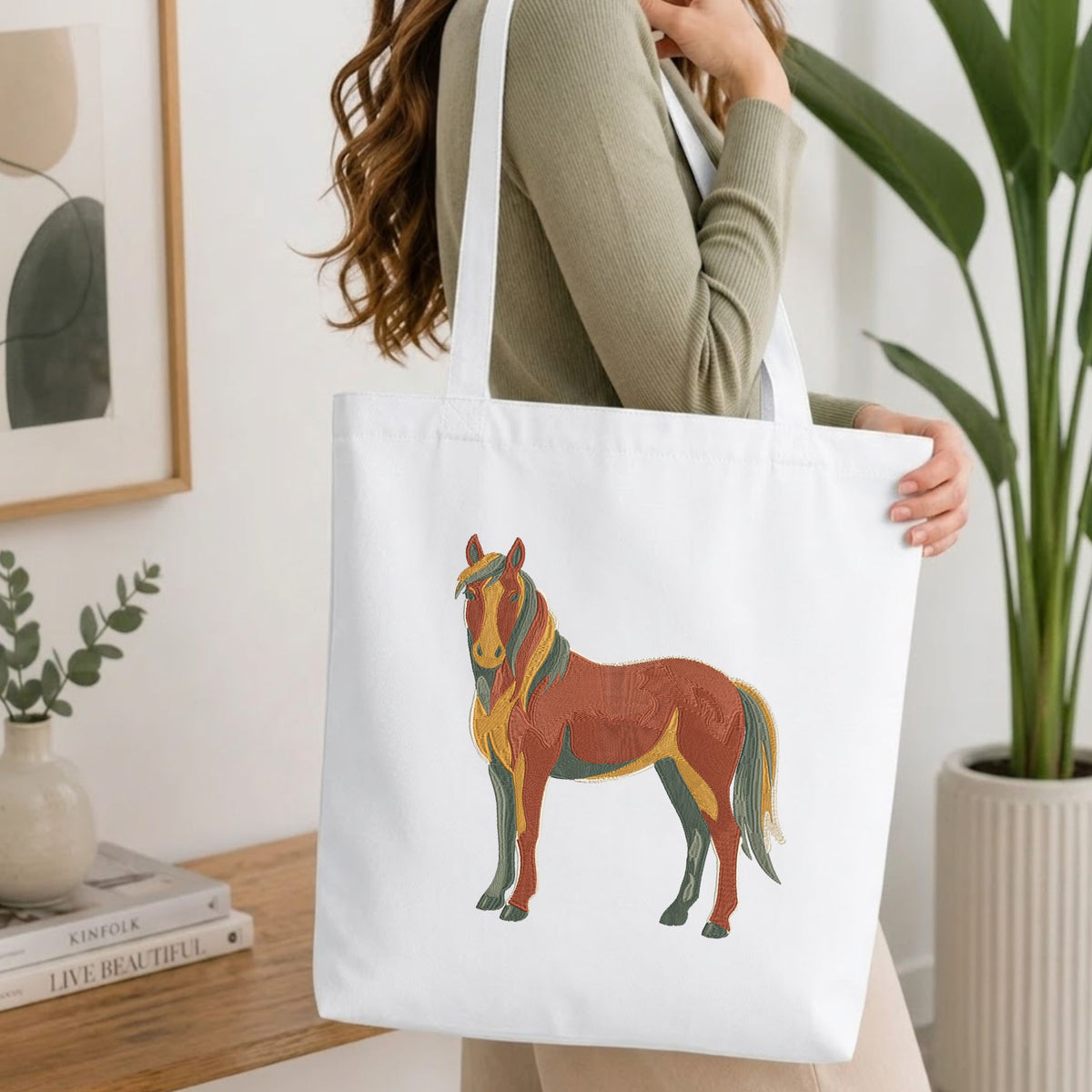 Folded white cotton t-shirt mockup featuring a colorful stylized horse machine embroidery design, styled with cotton stems and a wooden cup.