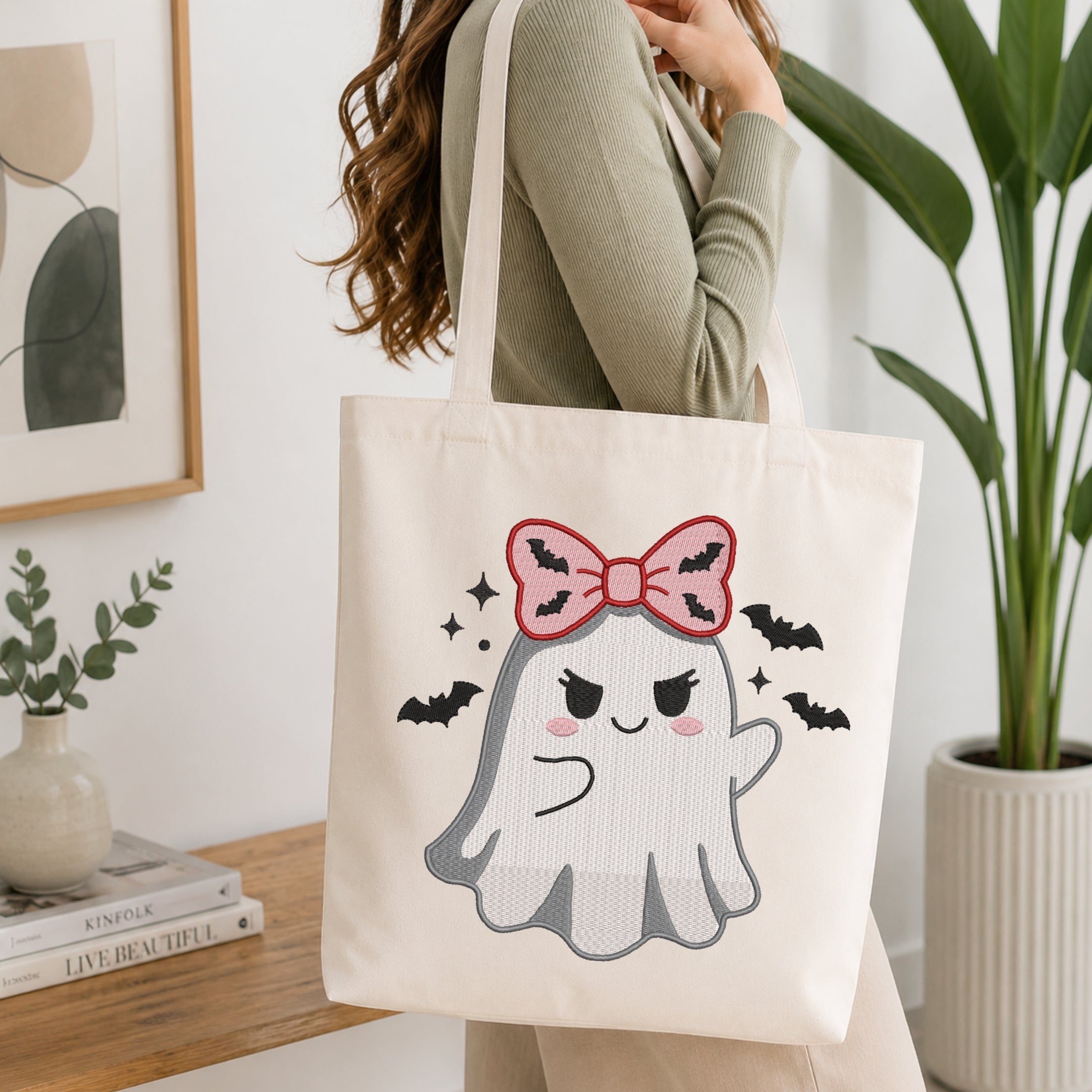 A person wearing a green long-sleeve top and carrying a natural canvas tote bag printed with the cute spooky ghost machine embroidery graphic.