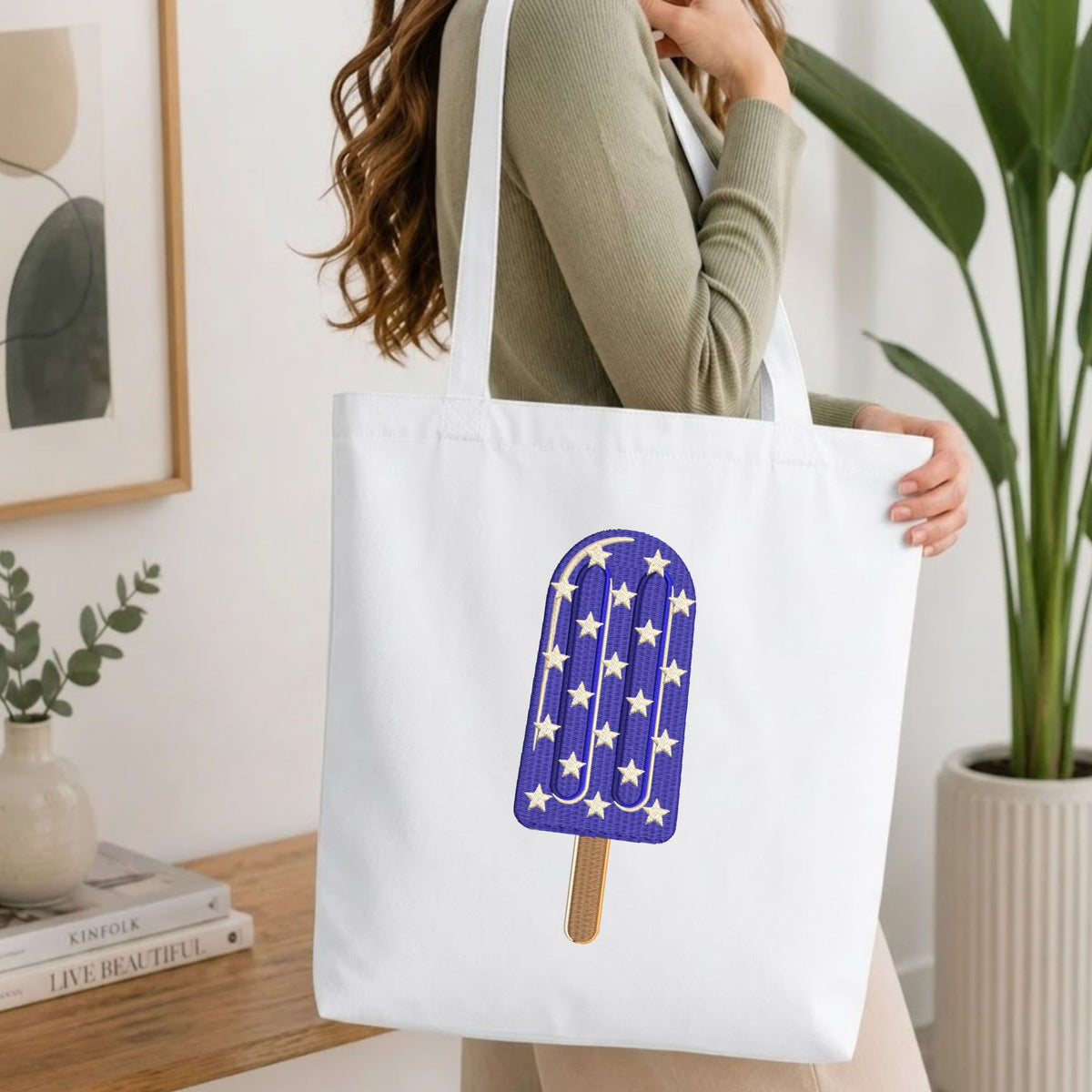  Woman carrying a white natural canvas tote bag featuring an embroidered purple star pattern ice cream popsicle design in a bright, modern interior setting.   