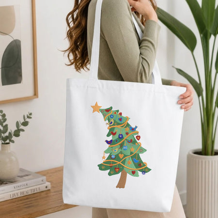Folded white cotton t-shirt mockup featuring a tilted Christmas tree machine embroidery design, styled with cotton stems and a wooden cup.