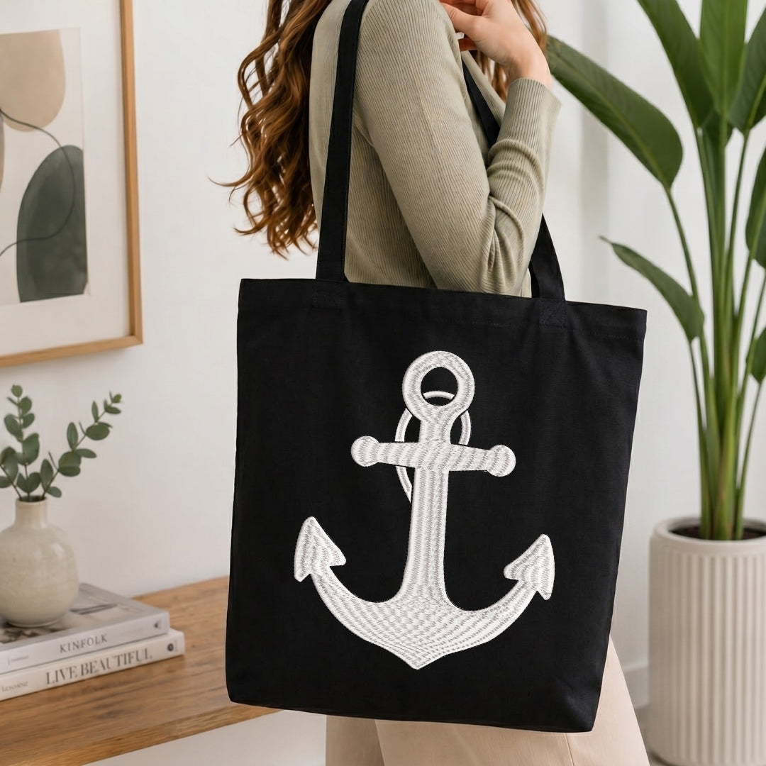 Person holding a black tote bag with a white anchor design in a home setting.