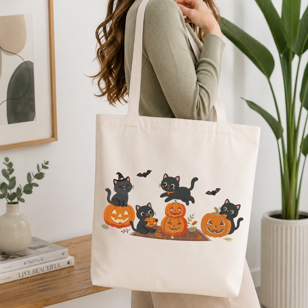 Woman carrying a white natural canvas tote bag featuring a cute black cats playing with jack-o-lantern pumpkins machine embroidery design in a bright, modern interior setting