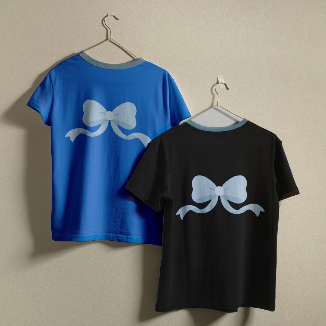 Two short-sleeve T-shirts hanging on hangers against a plain beige wall. The back of each shirt features a large light blue bow graphic, and both shirts have contrasting light blue ribbed trim at the collar.