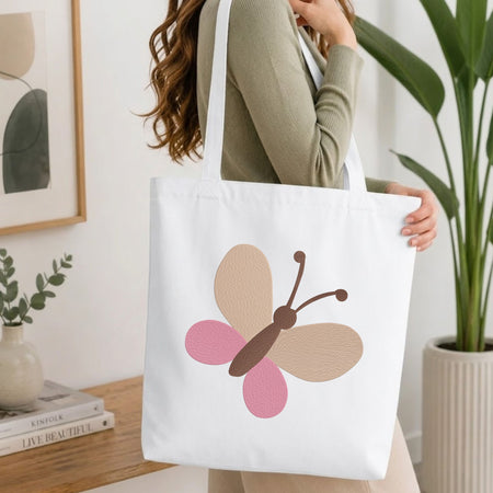 Woman carrying a white natural canvas tote bag featuring a minimalist butterfly machine embroidery design in a bright, modern interior setting