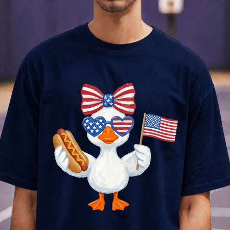 Person wearing a navy blue t-shirt with a patriotic duck design holding a hot dog and American flag.
