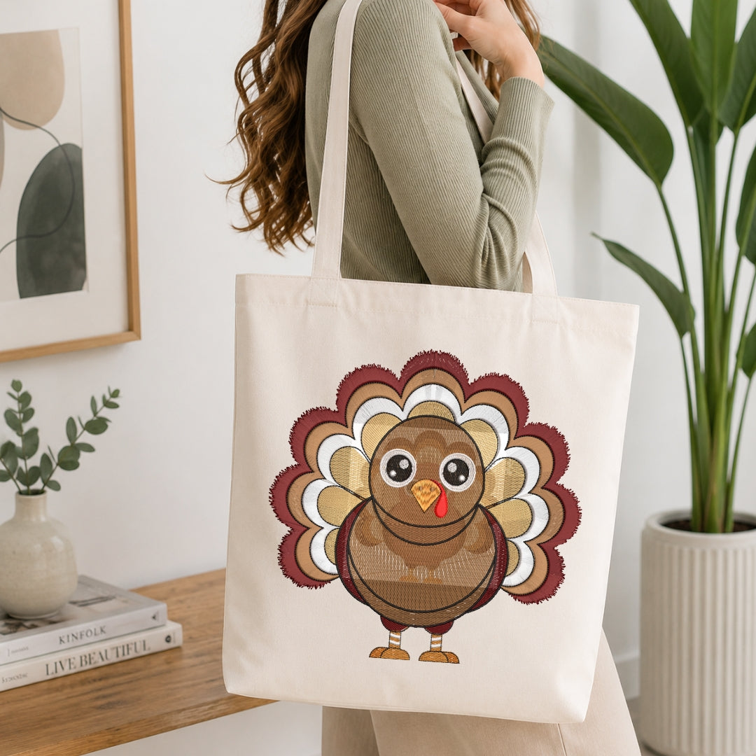 A person wearing a sage green ribbed long-sleeve top carries a cream canvas tote bag featuring a cute cartoon turkey design. The background is a bright, modern room with a wooden table, books, a framed print, and a potted plant.