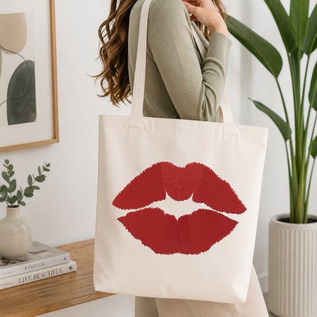 A person carrying a cream-colored canvas tote bag decorated with the embroidered red lips design.