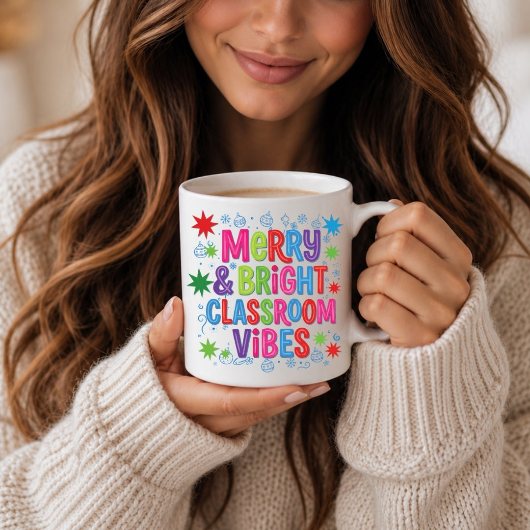 A woman in a cream knit sweater holds a white ceramic mug with colorful text reading 'Merry & Bright Classroom Vibes' surrounded by small star and cloud illustrations.