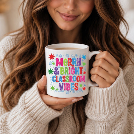 A woman in a cream knit sweater holds a white ceramic mug with colorful text reading 'Merry & Bright Classroom Vibes' surrounded by small star and cloud illustrations.