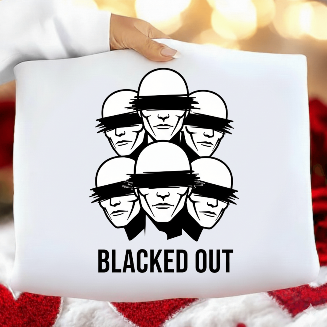 White pillow with black graphic design of faces with blindfolds and 'BLACKED OUT' text, held against a blurred background.